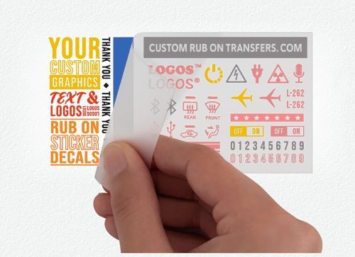 A hand peeling away a transparent transfer sheet from a white background. The Multi-Color Ensemble™ Transfer sheet ready to transfer in 1 application contains various red, yellow, and black custom graphics, texts, and logos including an airplane, audio waves, and numbers. The text "CUSTOM RUB ON TRANSFERS.COM" graces the top of this ready-to-transfer sheet.